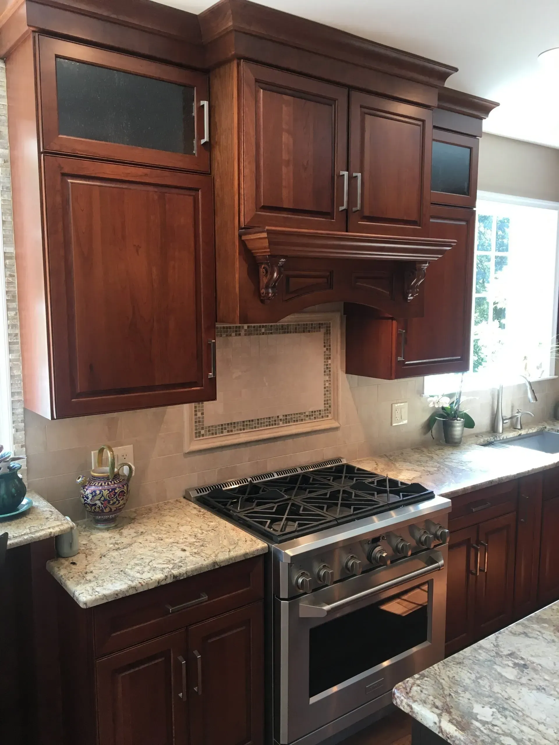 Kitchen with dark wood cabinets, granite counters, and stainless gas stove beside a sunlit window In Bucks Country PA