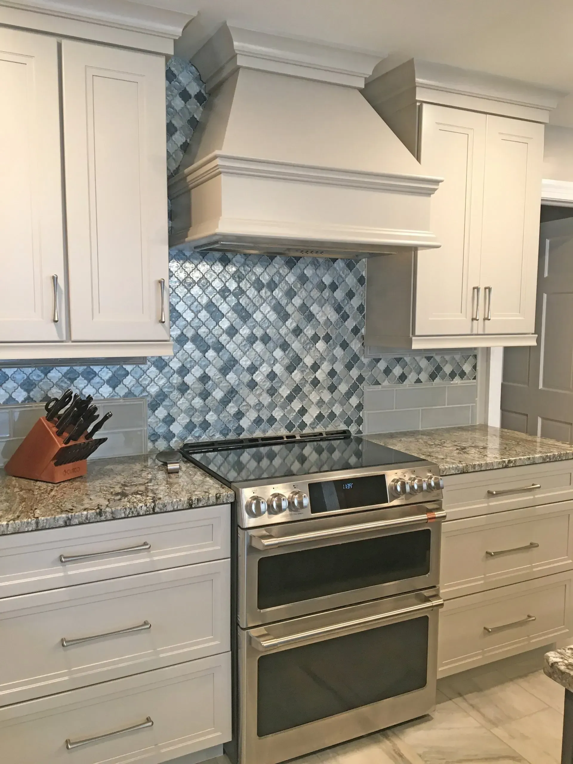 Modern kitchen with white cabinets, blue mosaic tile backsplash, granite counters, and stainless steel stove and hood  in Bucks County PA
