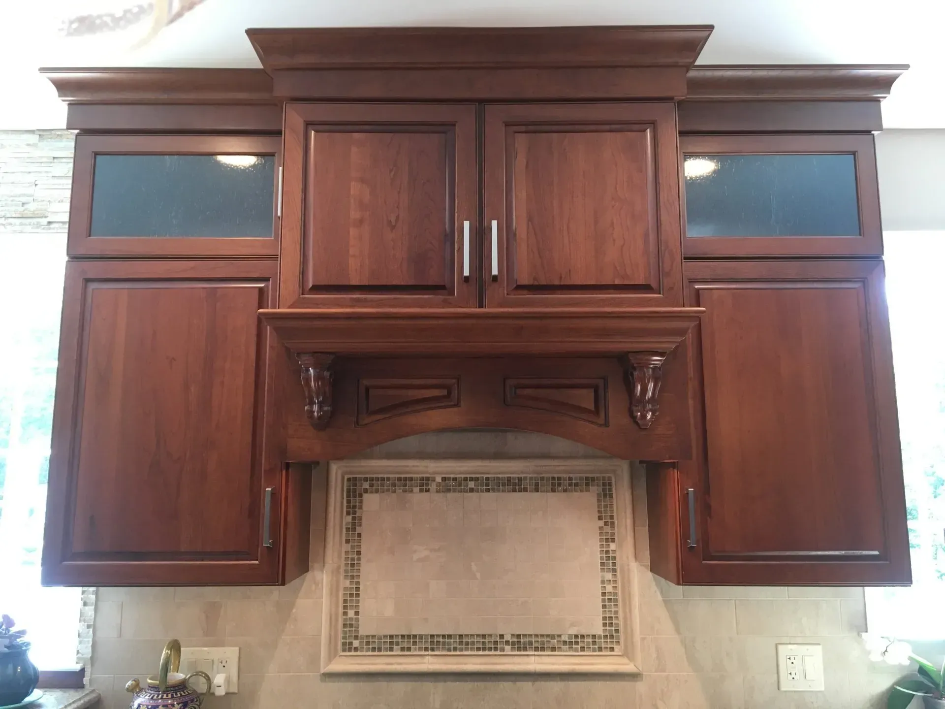 Wooden kitchen cabinets above a stove and tiled backsplash on a beige wall In Bucks Country PA