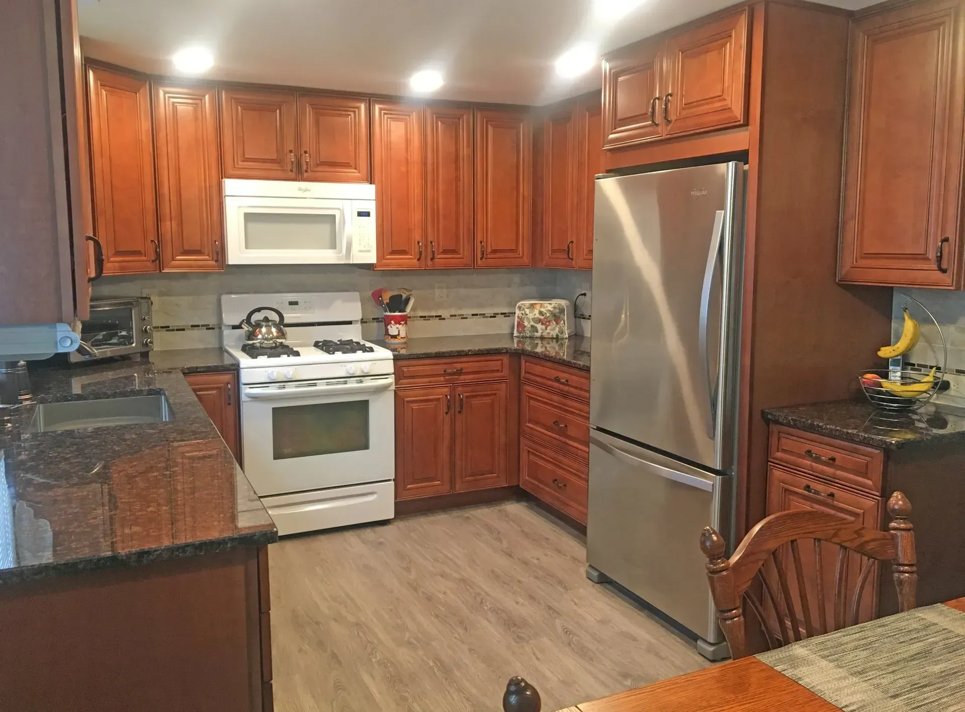 Modern kitchen with cherry cabinets, stainless refrigerator, white stove, and granite countertops In Bucks Country PA