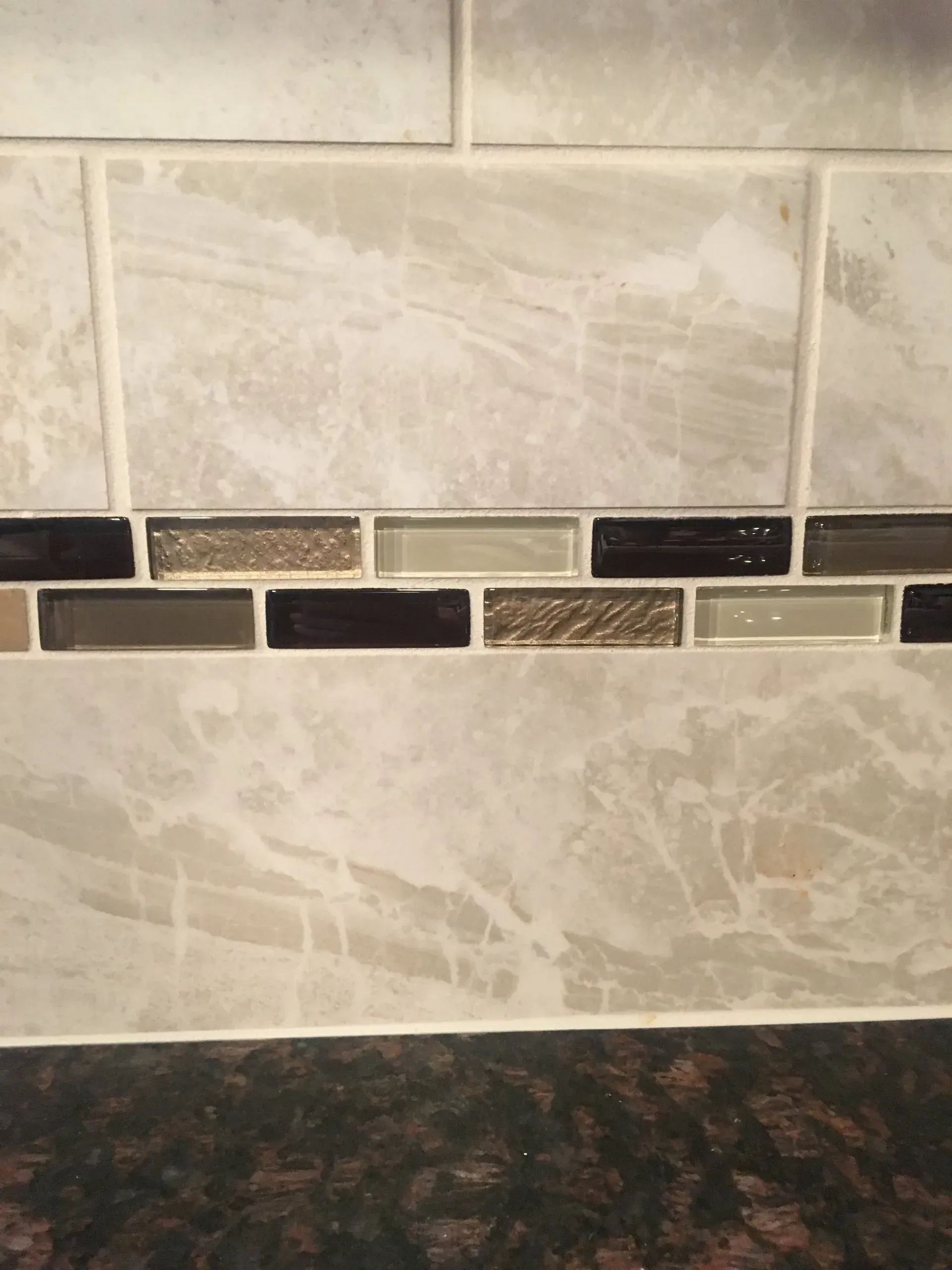 Beige tiled wall with a horizontal band of dark and mosaic accent tiles above a dark countertop In Bucks Country PA