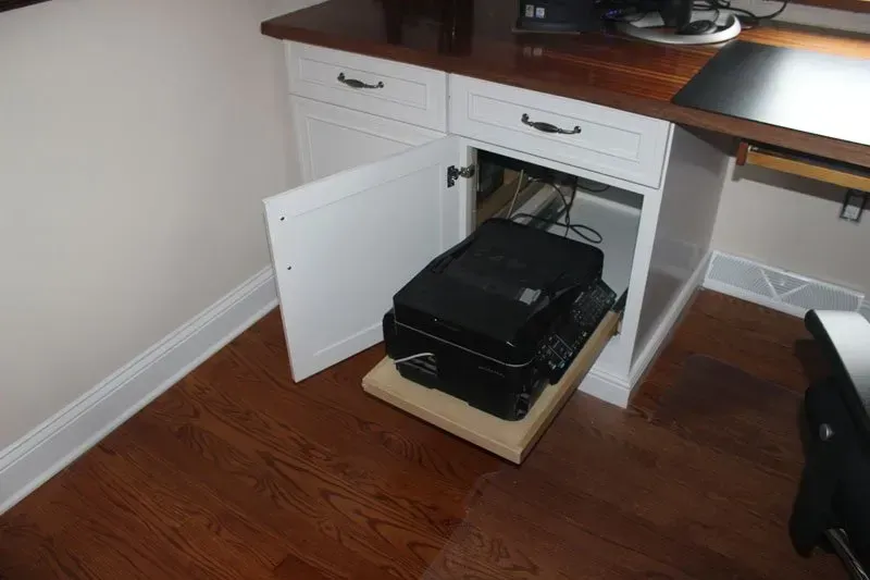 Open cabinet under desk revealing a black printer on a wooden pull-out tray in Bucks County PA