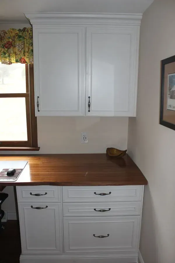 White kitchen cabinets and drawers above and below a wooden countertop beside a window in Bucks County PA