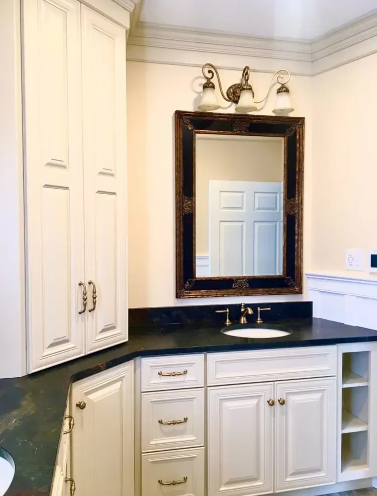 Elegant bathroom vanity with white cabinets, black countertop, and framed mirror with lights  In Bucks County PA