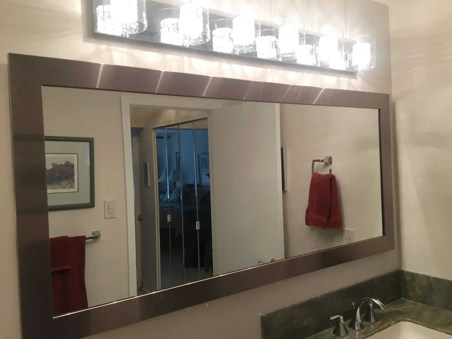 Bathroom mirror above sink with lights, reflecting a doorway and red towel on the wall  In Bucks County PA