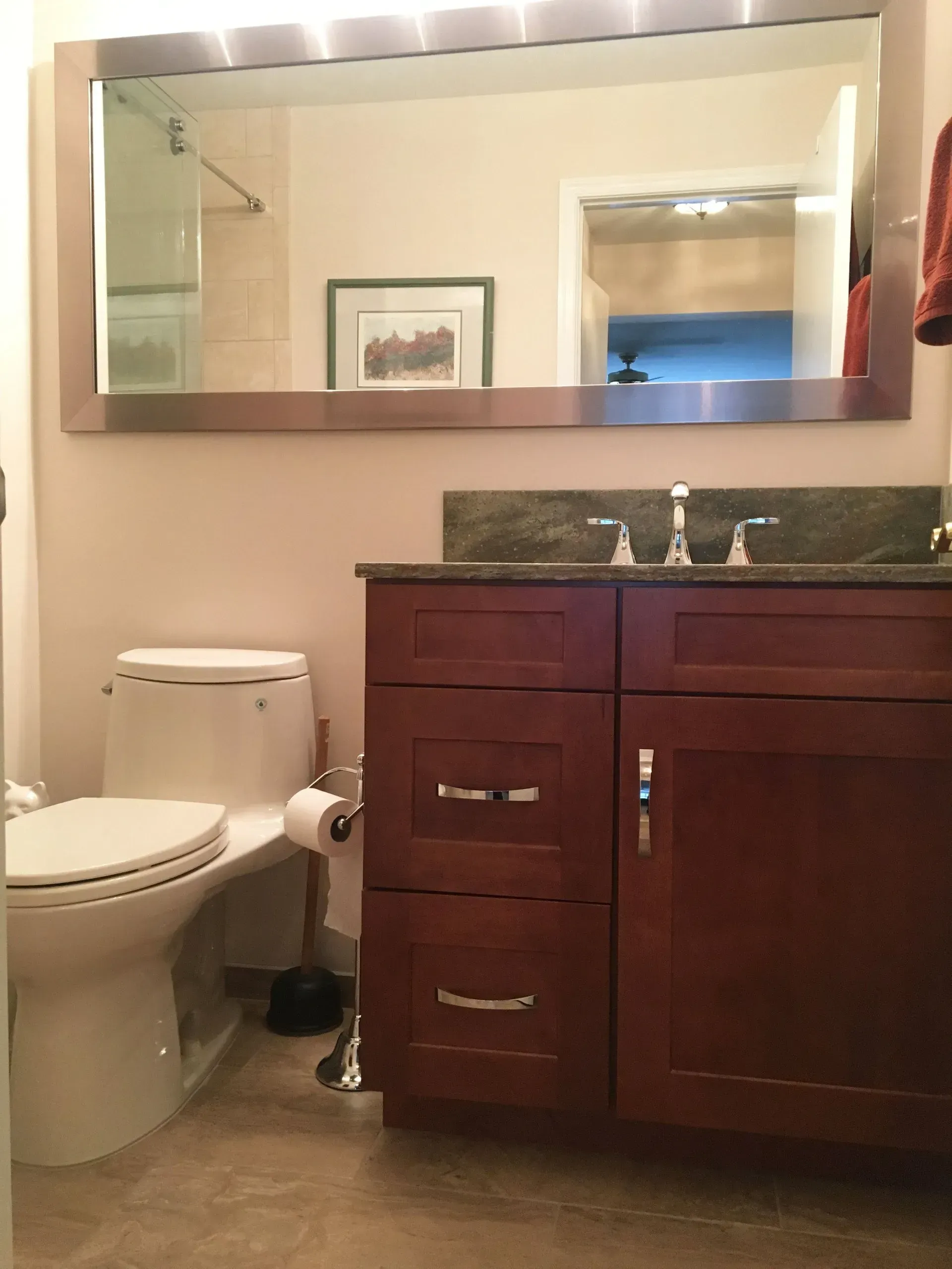 Small bathroom with toilet, dark wood vanity, sink, and large wall mirror  In Bucks County PA