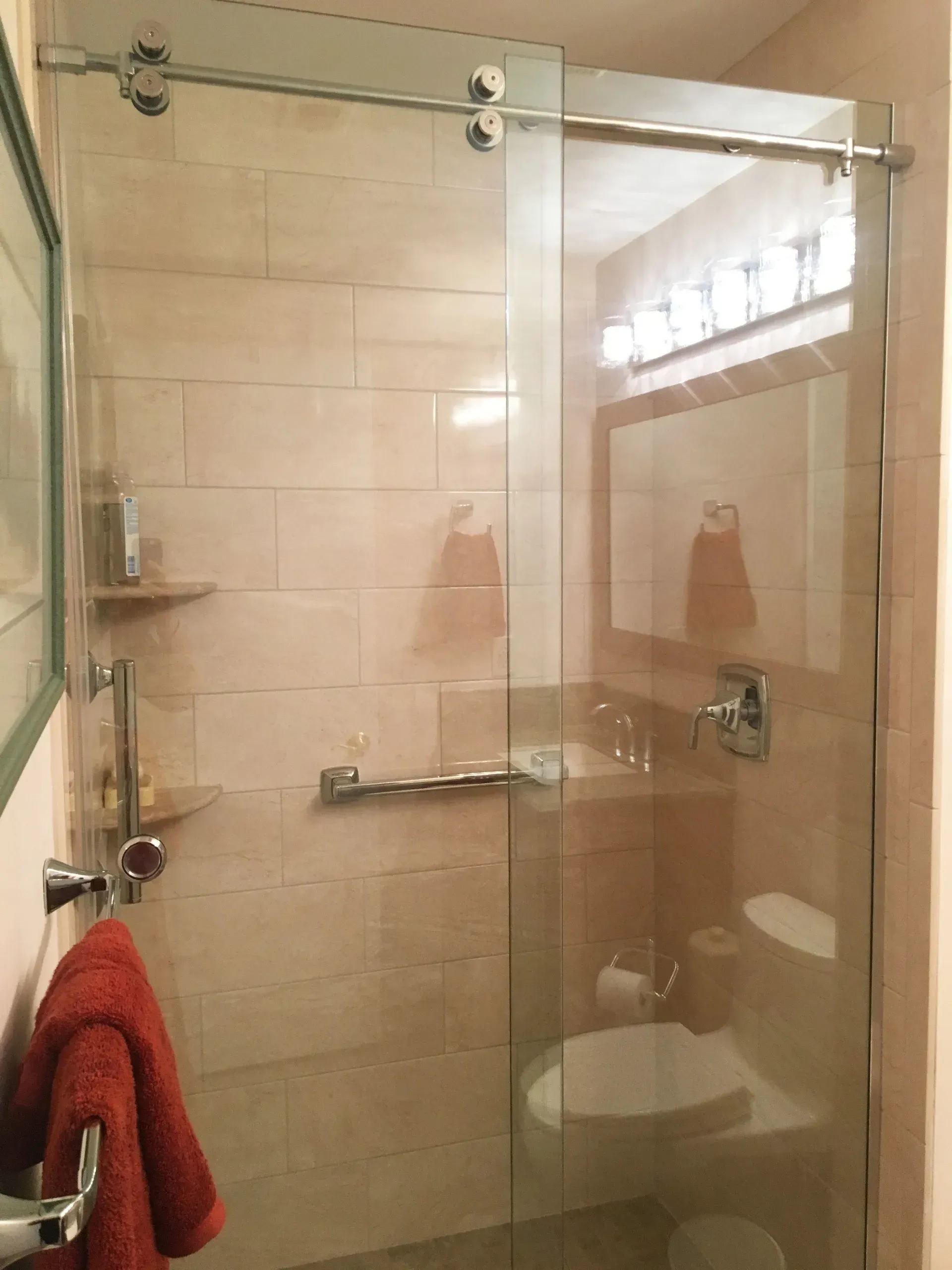 Small tiled bathroom with a glass shower enclosure, chrome fixtures, and red towels  In Bucks County PA