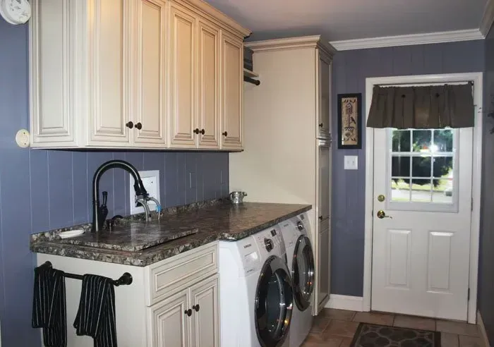 Laundry room with cream cabinets, black countertop, and white washer and dryer beside a back door In Bucks County PA