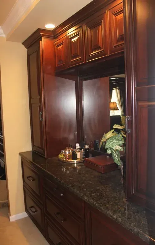 Dark wood vanity with mirror, granite countertop, and cabinet doors in a hallway alcove In Bucks County PA