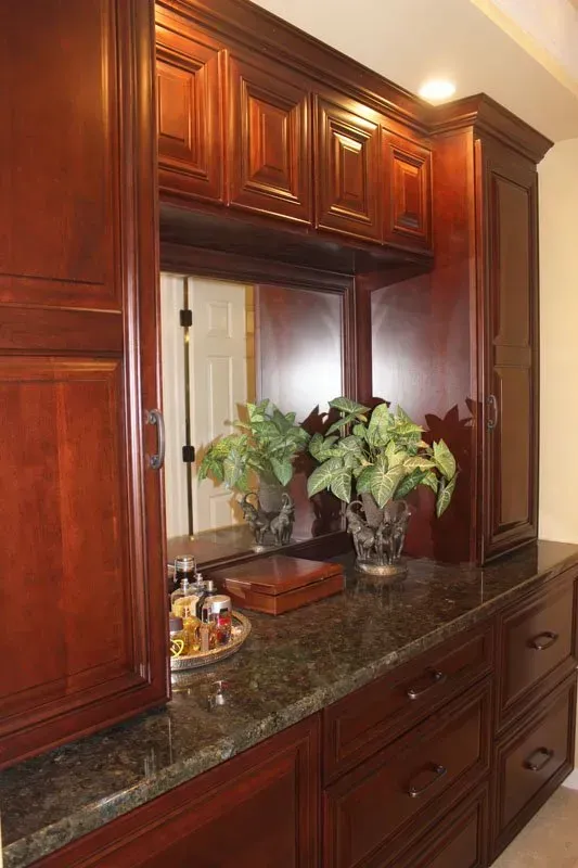 Dark wood bathroom vanity with granite countertop, mirror, and potted plants  In Bucks County PA