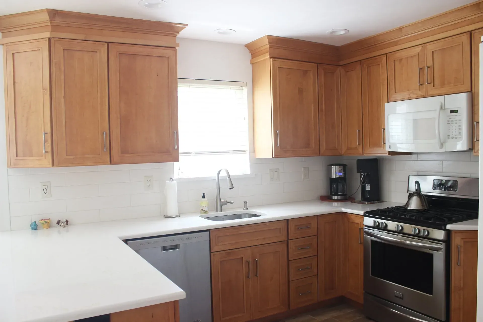 Bright kitchen with wooden cabinets, white countertops, stainless steel stove, and a window over the sink  In Bucks County PA