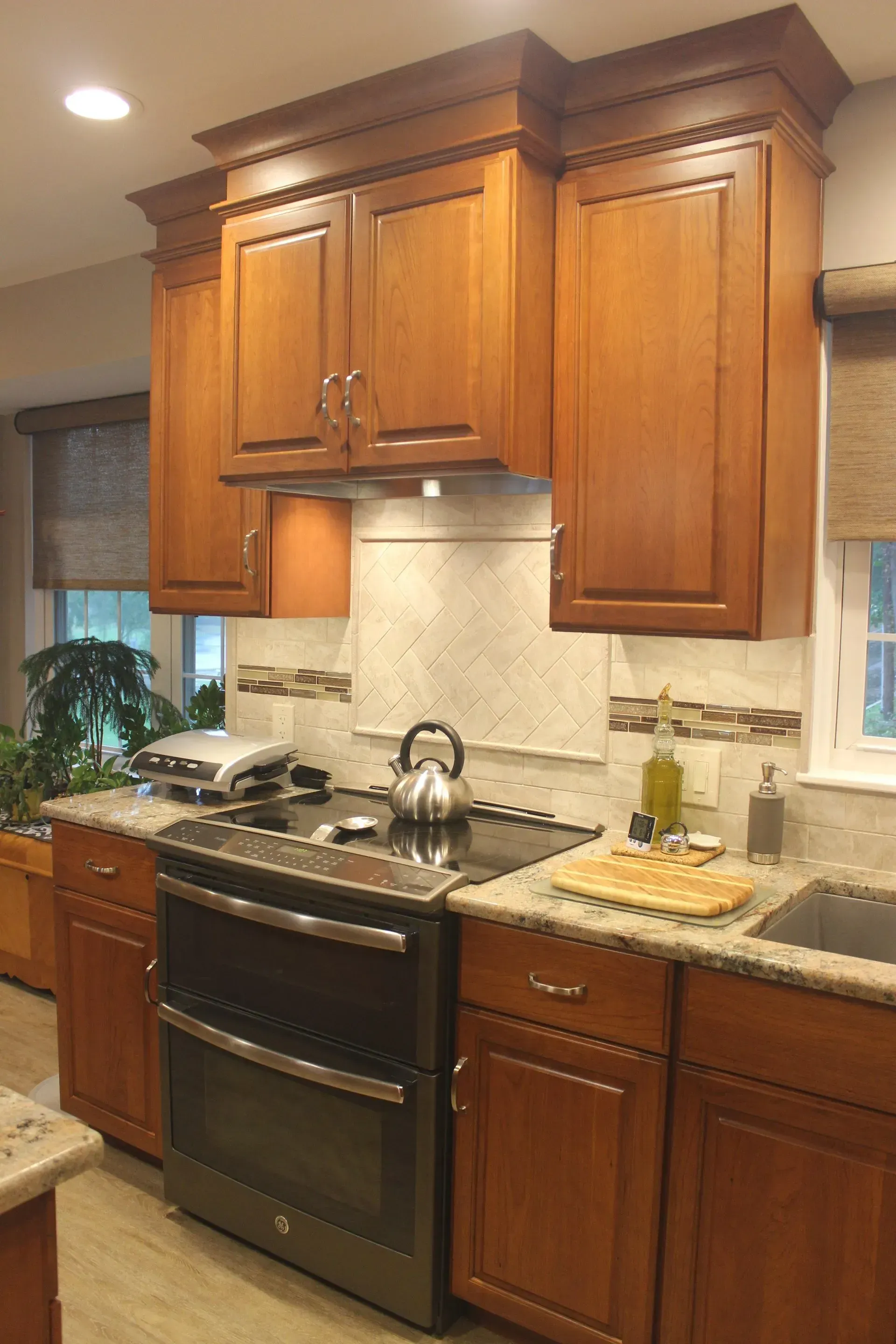 Wooden kitchen cabinets above a black stove and granite countertop, with tiled backsplash and window light In Bucks County PA