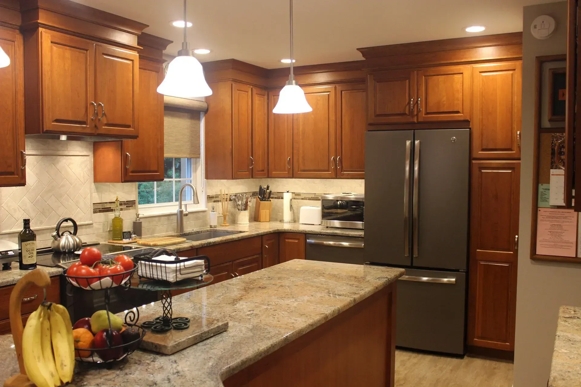 Modern kitchen with wooden cabinets, granite island, stainless steel fridge, and pendant lights In Bucks County PA