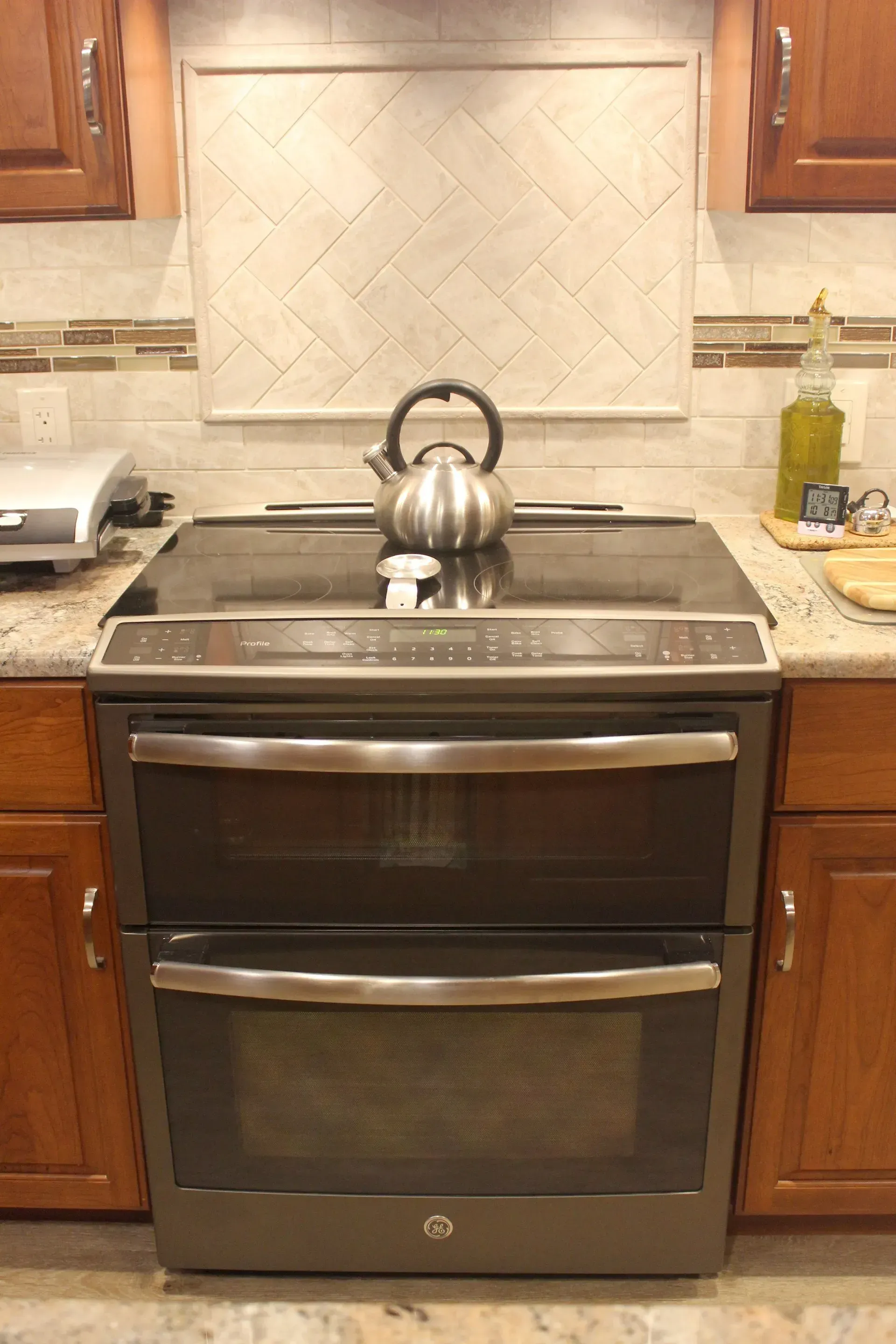 Kitchen stove with a kettle on the cooktop, framed by wood cabinets and beige countertops In Bucks County PA