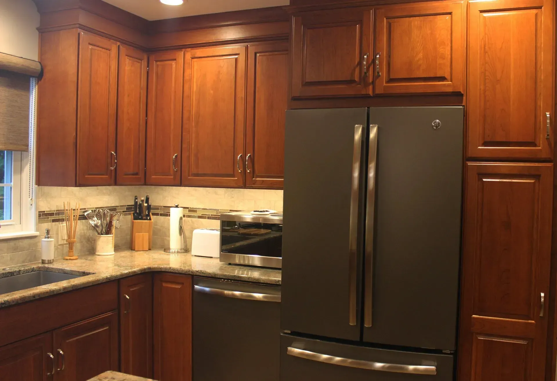 Kitchen with dark wood cabinets, black refrigerator, and granite countertop under warm lighting In Bucks County PA