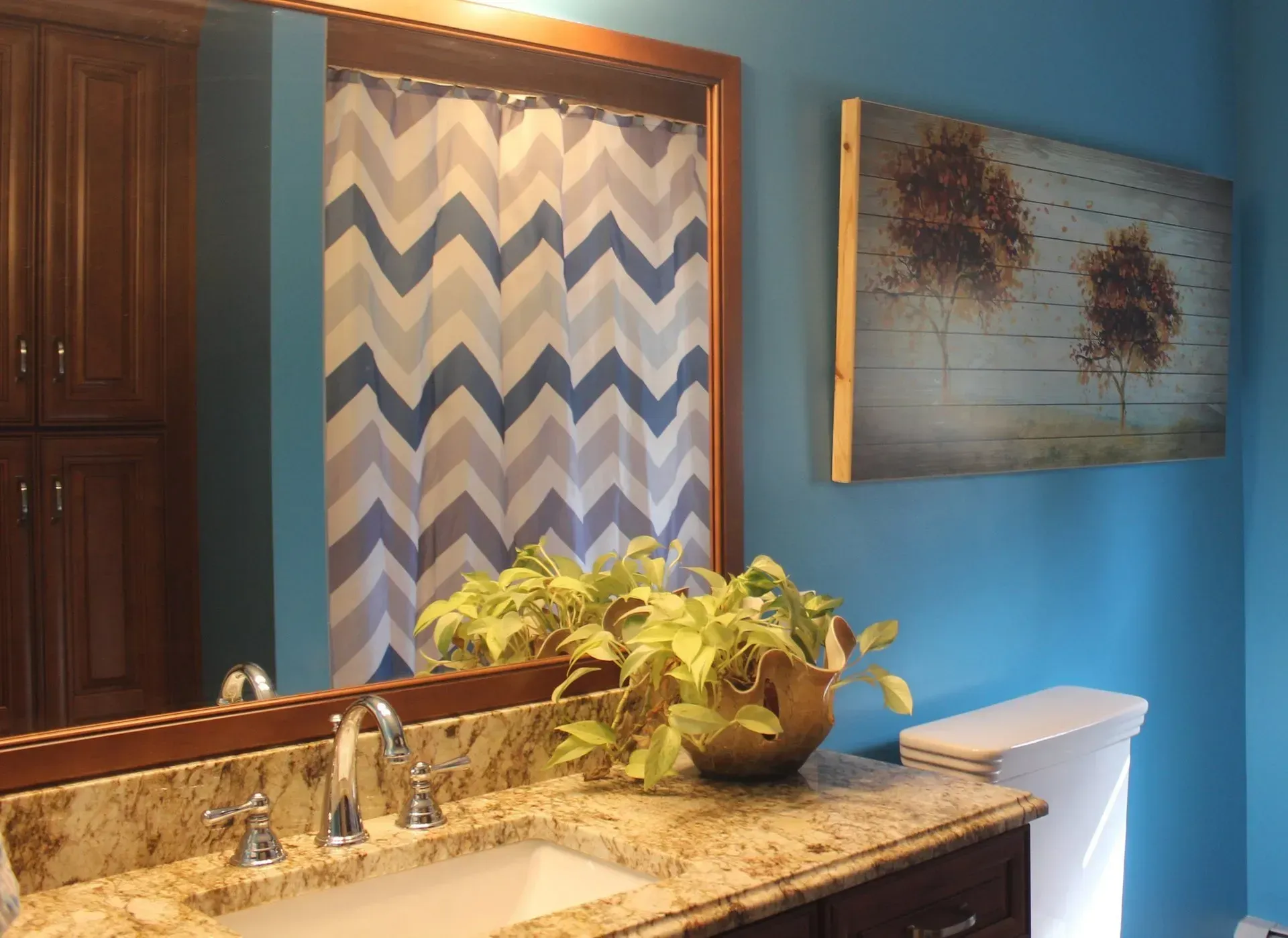 Bathroom vanity with granite countertop, sink, mirror, blue walls, patterned shower curtain, and wall art  In Bucks County PA
