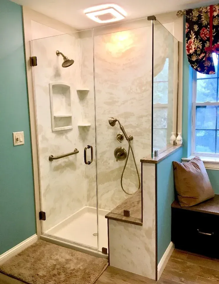 Walk-in shower with glass door, white tile, built-in bench, and window seat beside it  In Bucks County PA
