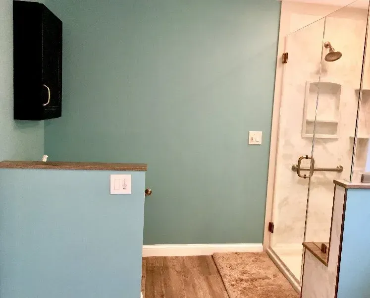 Empty bathroom with teal walls, wood floor, and a glass shower enclosure  In Bucks County PA