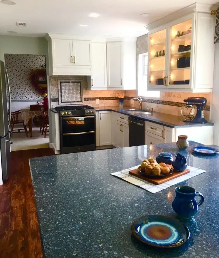 Bright kitchen with white cabinets, black stove, blue-speckled island countertop, and lit glass display cabinet In Bucks County PA