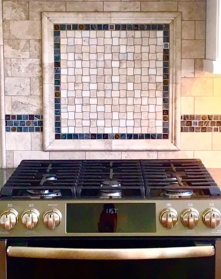 Stainless steel gas stove beneath a beige tiled backsplash with small mosaic accents In Bucks County PA