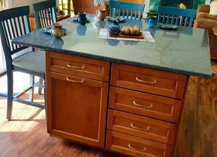 Kitchen island with green countertop, wooden cabinets, and stools around a dining table In Bucks County PA
