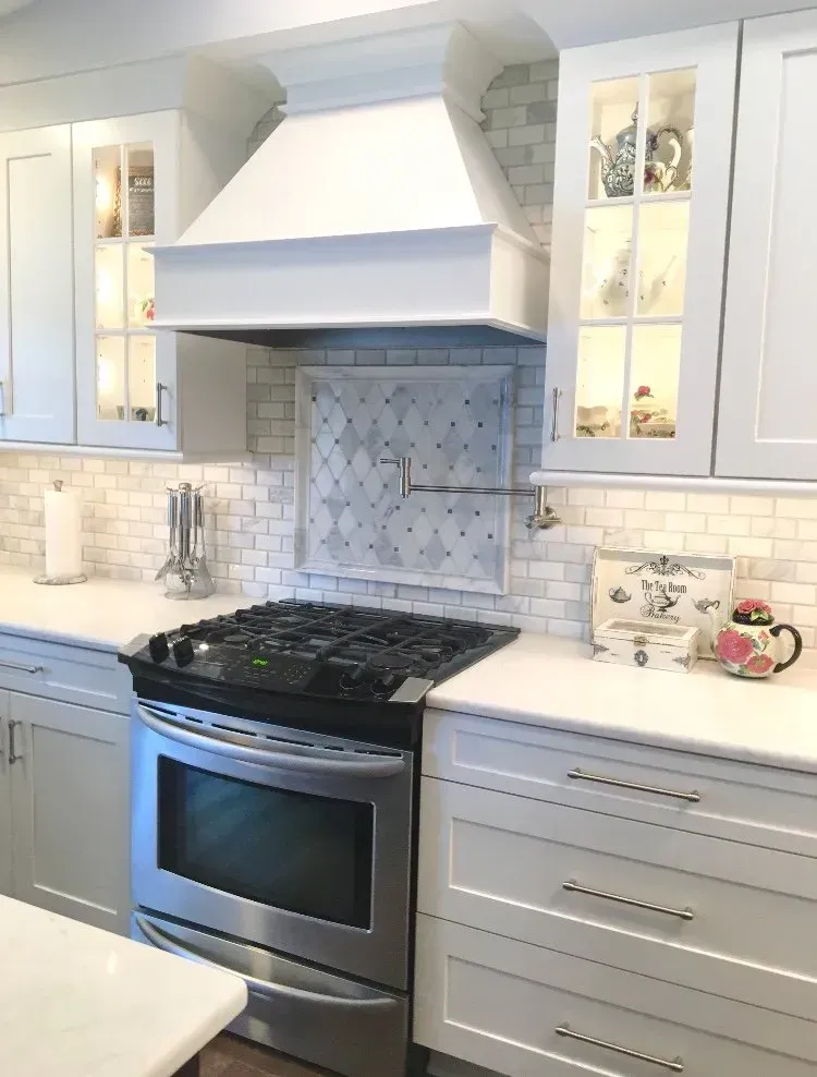 Bright white kitchen with stainless steel stove, ornate range hood, and glass-front cabinets In Bucks Country PA