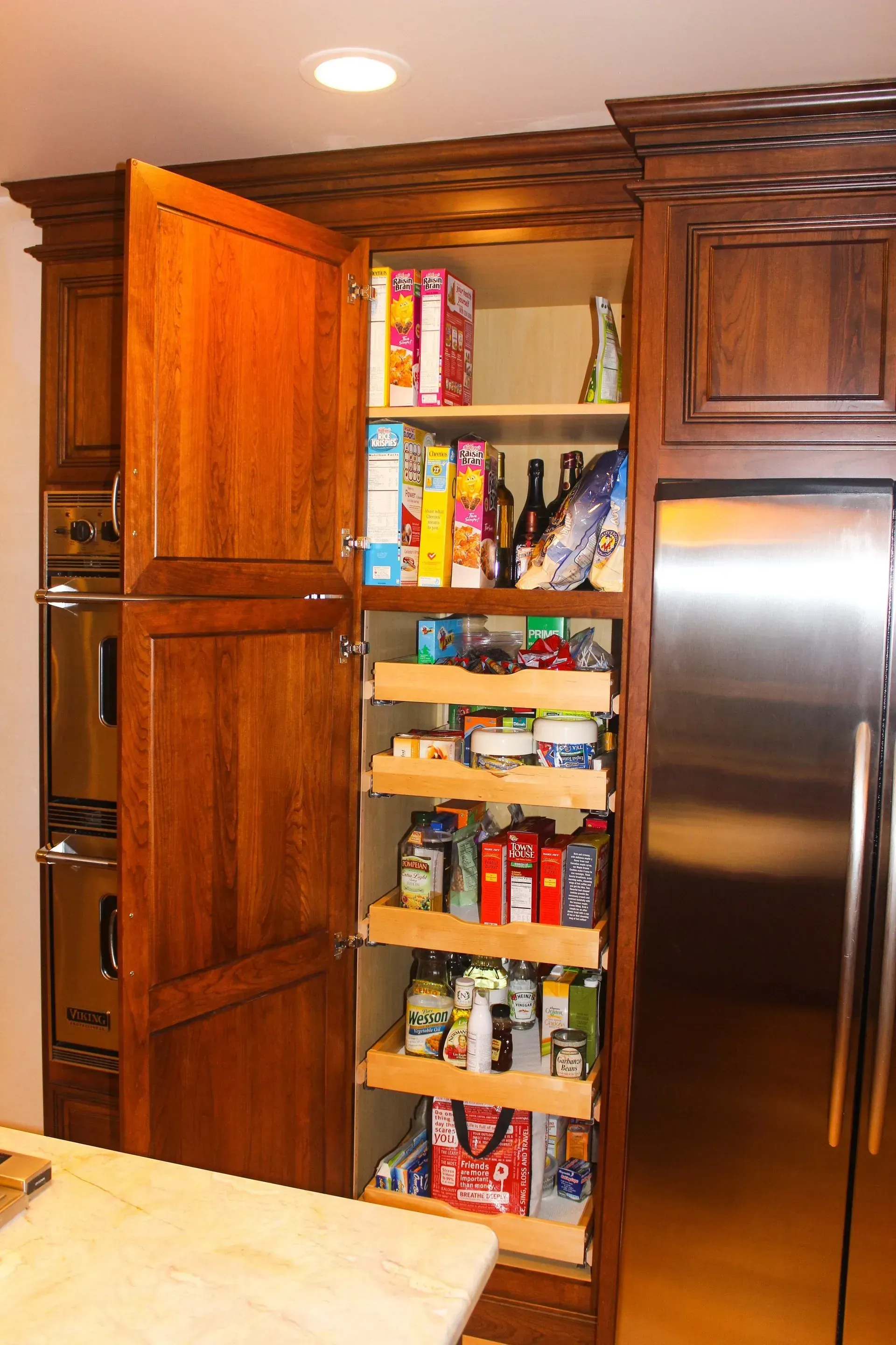 Open pantry cabinet filled with snacks beside a stainless steel refrigerator in a kitchen In Bucks Country PA