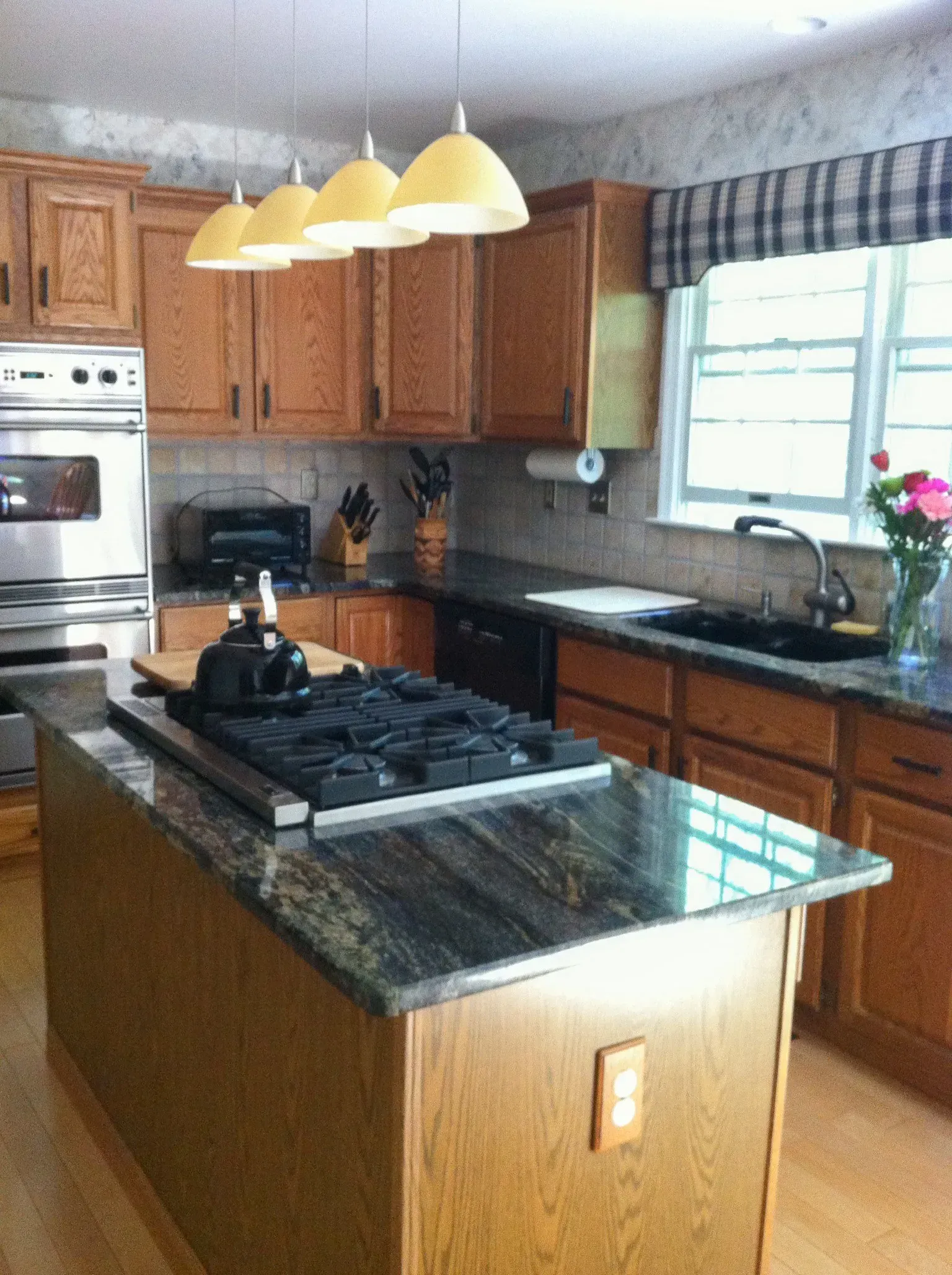 Bright kitchen with wooden cabinets, granite island, hanging lights, and a window over the sink.In Bucks Country PA