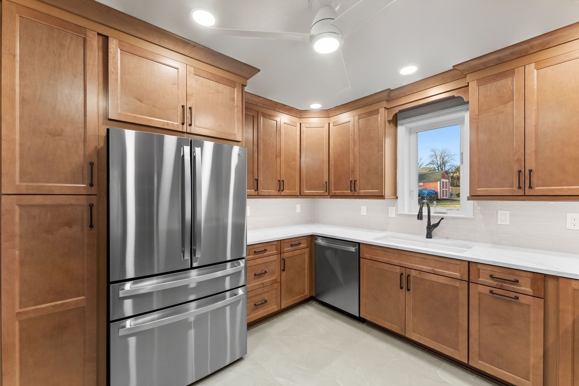 Modern kitchen with stainless steel refrigerator, wood cabinets, white backsplash, and a window over the sink  In Bucks County PA