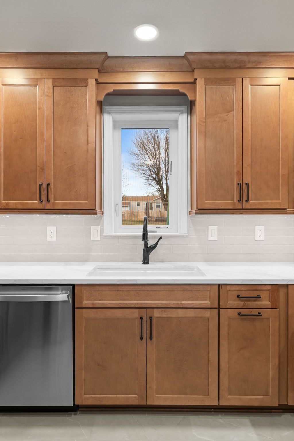 Kitchen sink under a window, flanked by light wood cabinets and a black faucet; dishwasher on left  In Bucks County PA