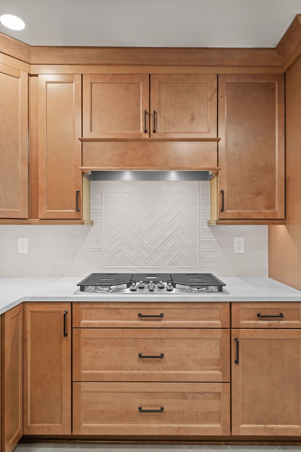Kitchen with light wood cabinets, white backsplash, and stainless gas cooktop beneath a vent hood  In Bucks County PA