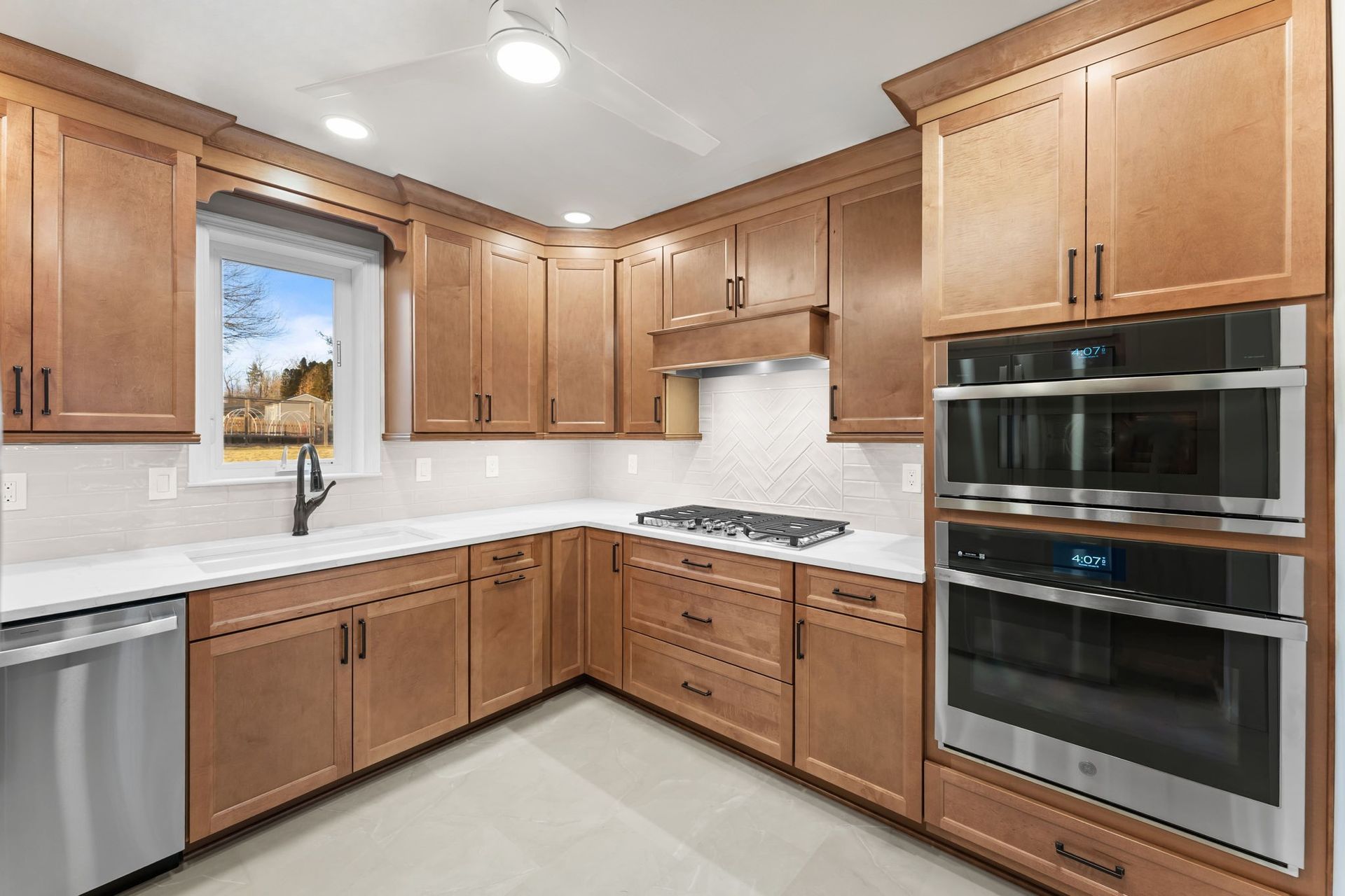 Modern kitchen with wooden cabinets, white countertops, double oven, gas range, and window above the sink  In Bucks County PA