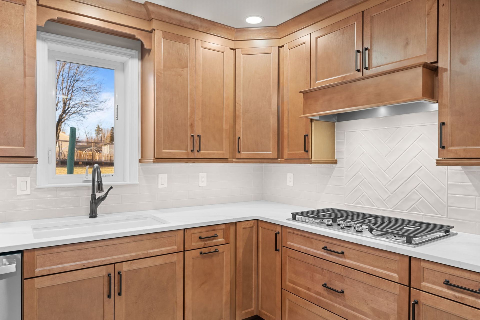 Wooden kitchen cabinets, white countertops, and a gas cooktop beneath a tiled backsplash  In Bucks County PA