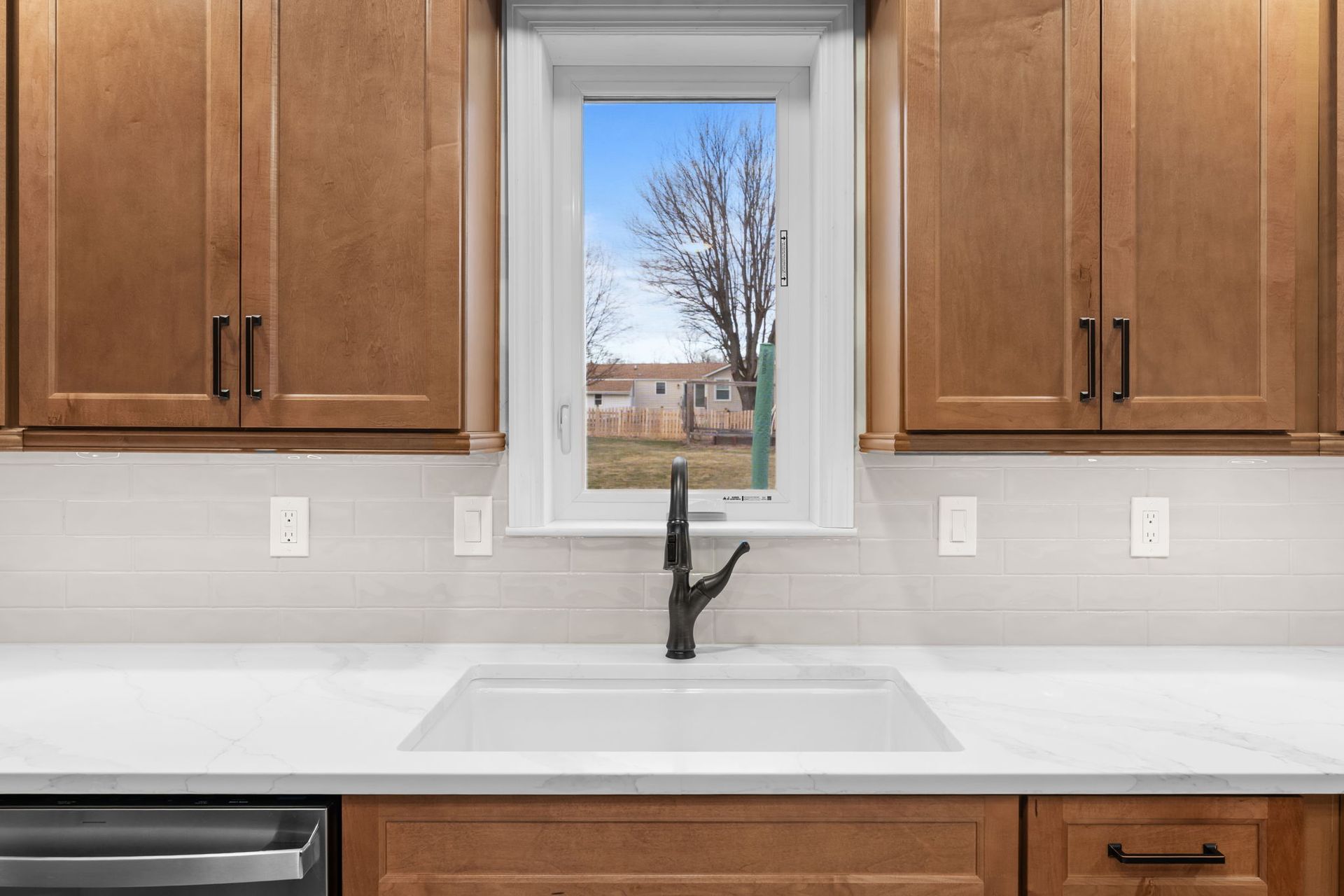 Kitchen sink beneath a window with wood cabinets and a black faucet, showing a snowy yard outside In Bucks County PA