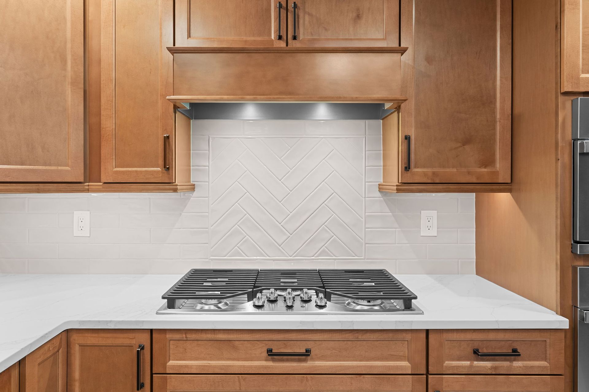 Kitchen countertop with a gas cooktop, white backsplash, and wooden cabinets  In Bucks County PA