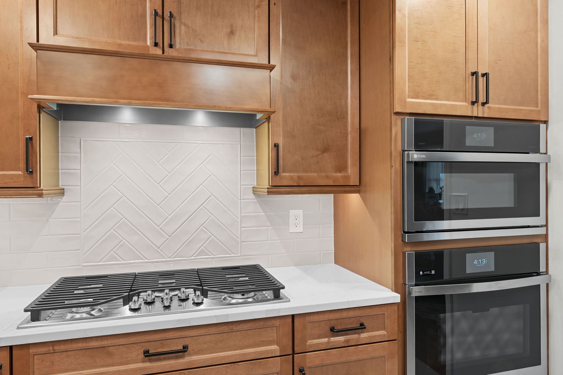 Kitchen with wooden cabinets, gas cooktop, white backsplash, and built-in double oven  In Bucks County PA