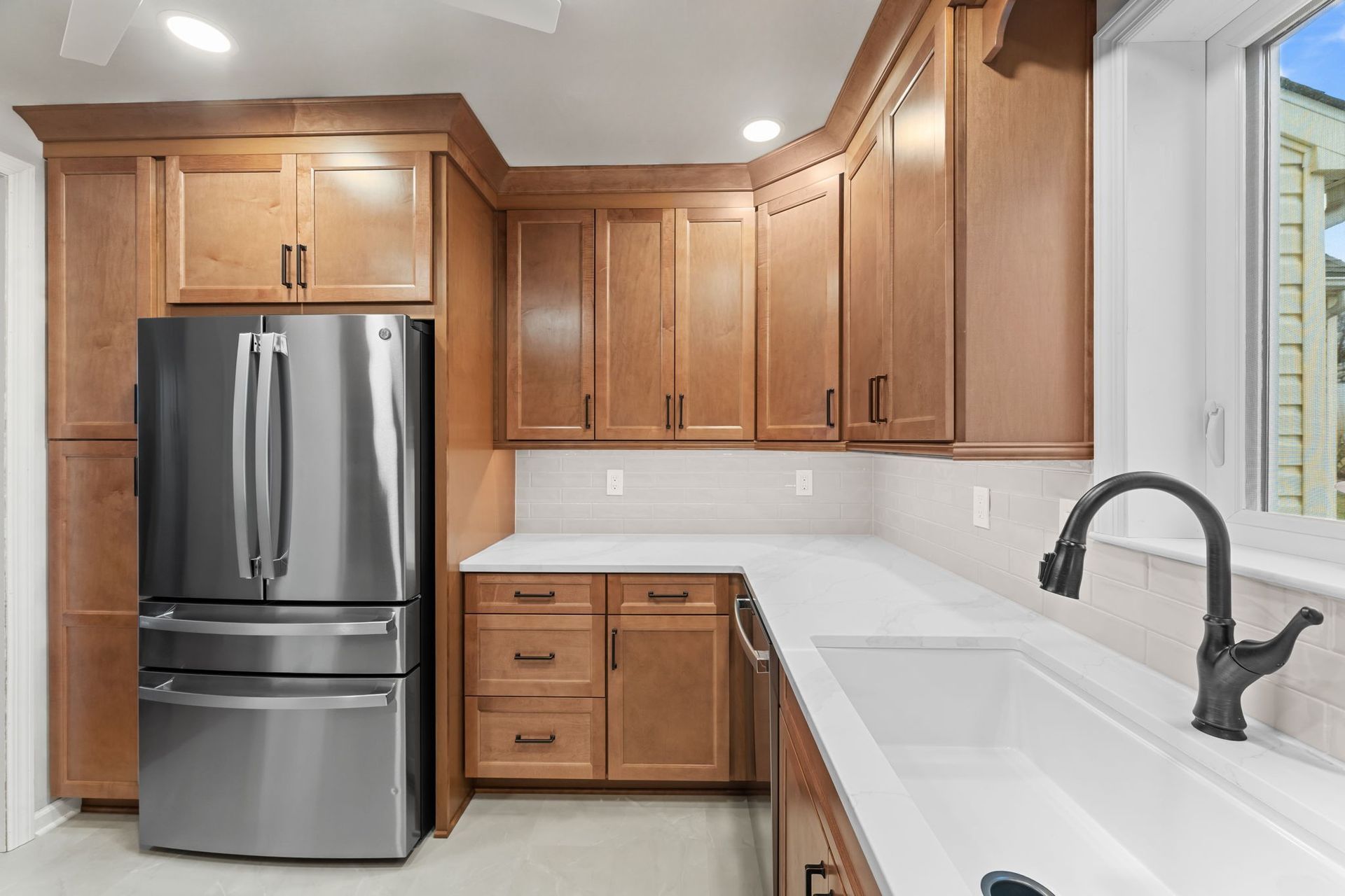 Modern kitchen with stainless steel fridge, light wood cabinets, white counters, and black faucet In Bucks County PA
