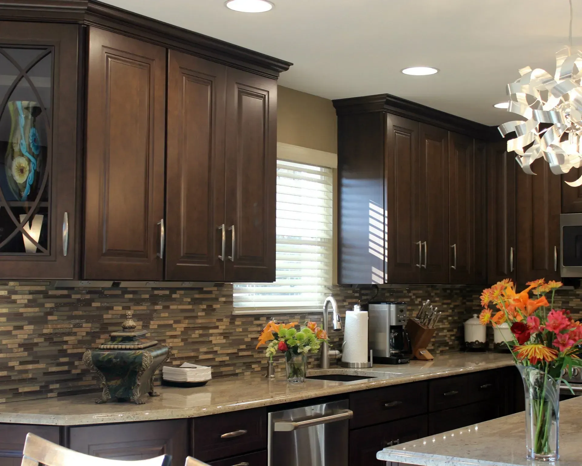 Modern kitchen with dark wood cabinets, mosaic backsplash, granite counters, and a flower arrangement on the island  In Bucks County PA