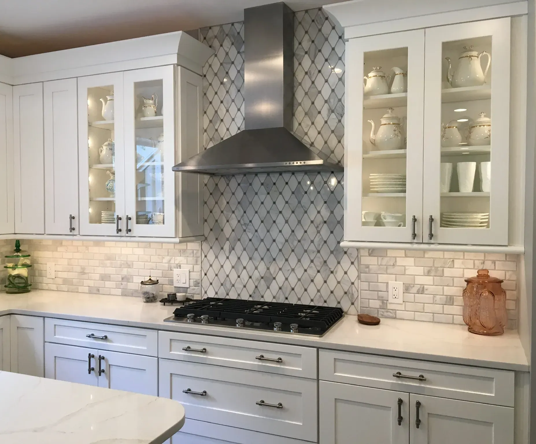 Modern white kitchen with gray tile backsplash, glass cabinets, stainless range hood, and gas stove In Bucks County PA