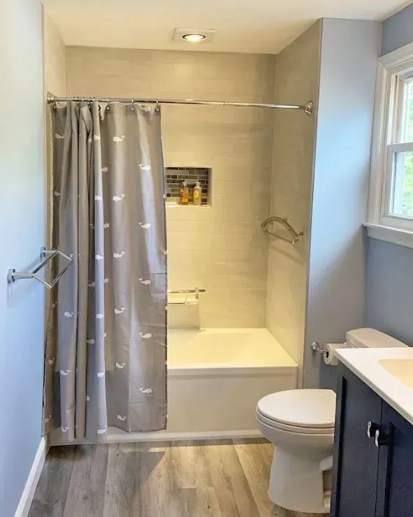 Small bathroom with shower curtain, bathtub, toilet, sink, and window In Bucks Country PA