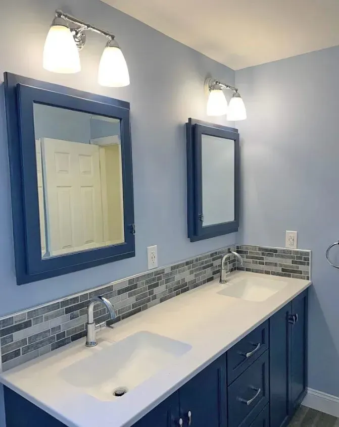 Blue bathroom vanity with double sinks, large mirror, wall sconces, and mosaic backsplash In Bucks Country PA