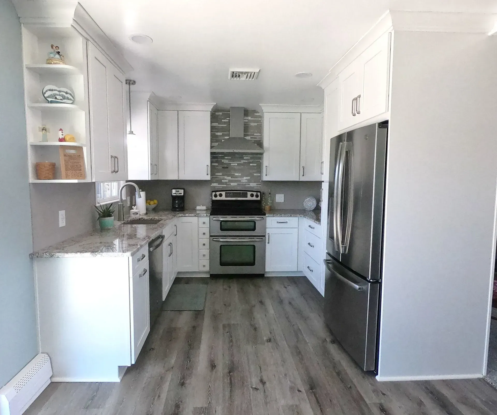 Modern white kitchen with gray backsplash, stainless appliances, and wood-look flooring In Bucks Country PA