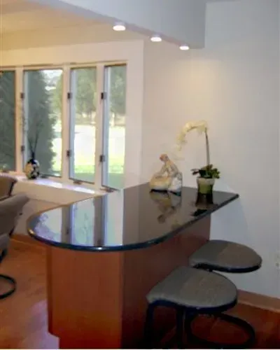 Modern kitchen with curved black countertop, bar stools, sink, and large windows overlooking greenery in Bucks County PA