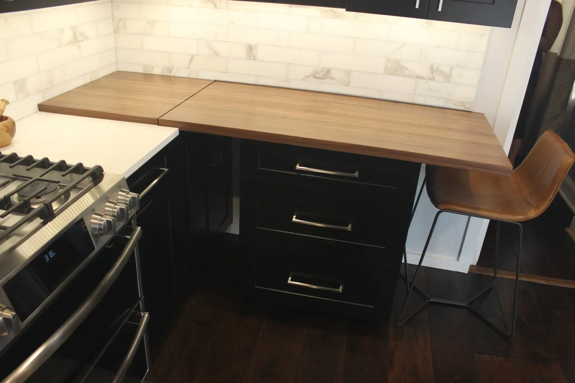 Modern kitchen with wooden countertops, black cabinets, stove, and a wooden chair by the counter in Bucks County PA