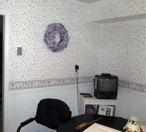 Small room with patterned wallpaper, black chair, desk, old TV, and a purple wall decoration In Bucks County PA