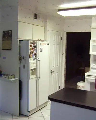 Small kitchen with a white refrigerator, cabinets, and a dark countertop; doorway leads to a dim adjacent room in Bucks County PA 