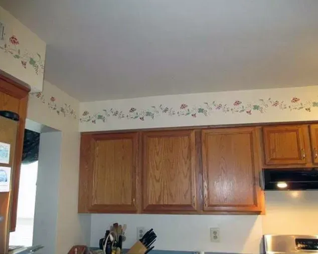 Kitchen with wooden cabinets, white walls, floral border wallpaper, and a stove at right  In Bucks County PA