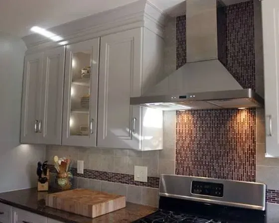 Modern kitchen with white cabinets, stainless steel range hood, mosaic backsplash, and wood countertop  In Bucks County PA
