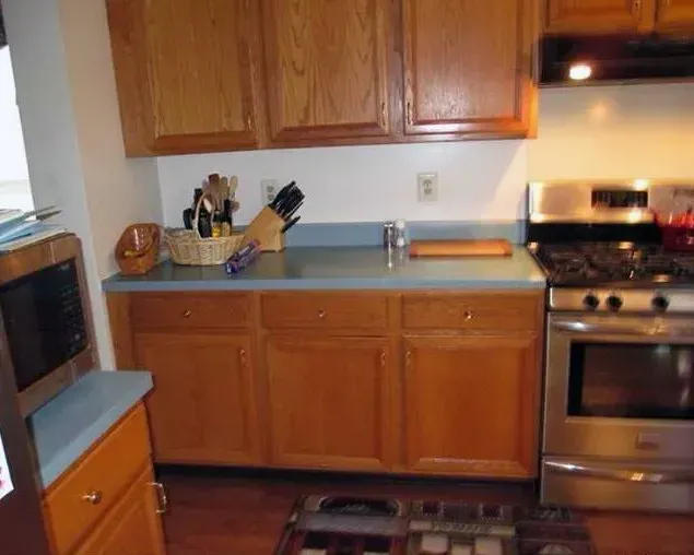 Kitchen with wooden cabinets, blue countertop, stainless steel stove, and a window on the left In Bucks County PA