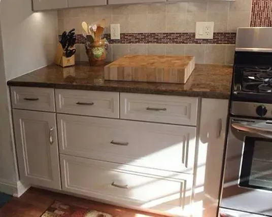 Modern kitchen counter with white cabinets, dark countertop, wood cutting board, and tiled backsplash  In Bucks County PA